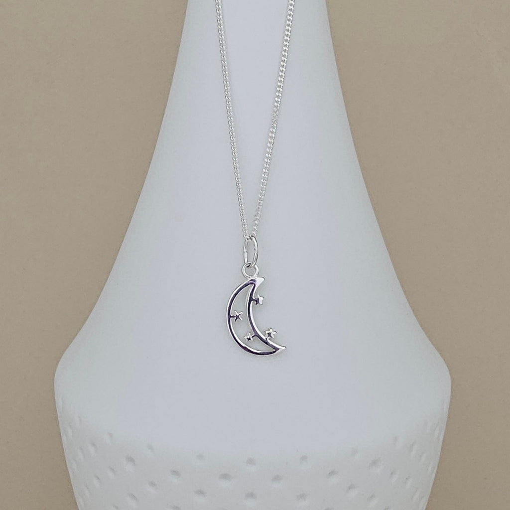 A silver crescent moon and star pendant necklace displayed on a white ceramic vase against a beige background.