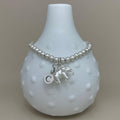 A silver beaded bracelet with a small elephant charm, a letter C initial charm, and a round charm, displayed on a white textured ceramic vase against a neutral beige background.