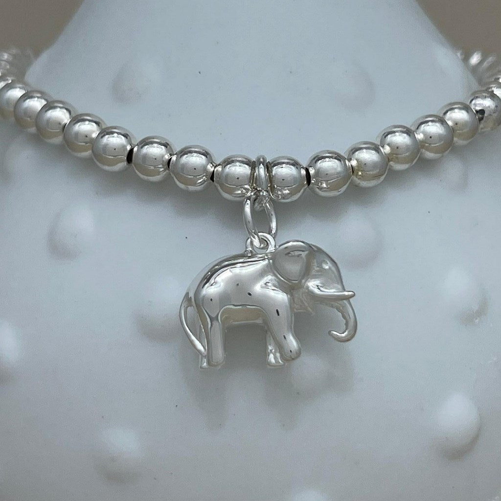 A silver beaded bracelet with a small elephant charm, displayed on a white textured bust.