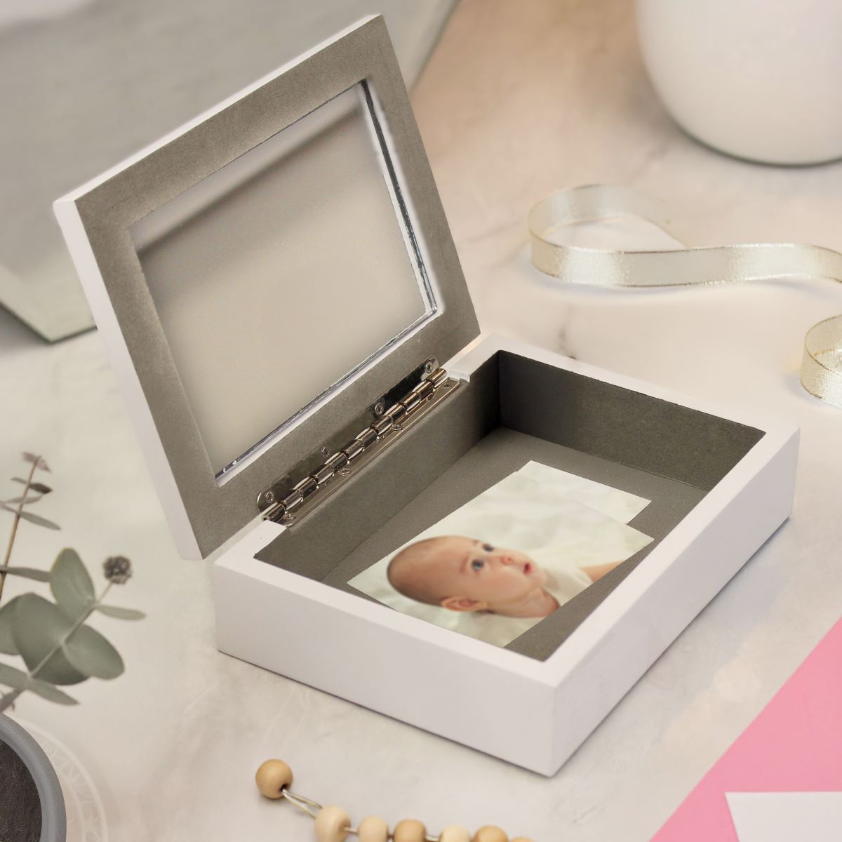 White jewelry box with a photo of a baby inside, on a light surface.