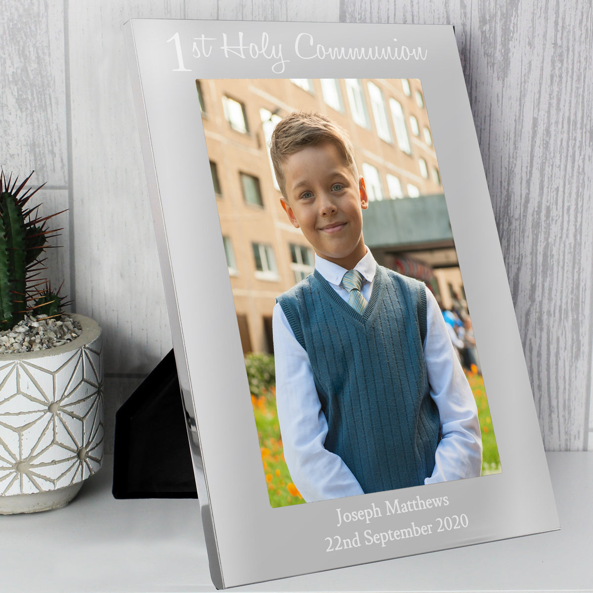 Silver photo frame with a young boy's picture and text, placed on a wooden surface with a plant in the background.