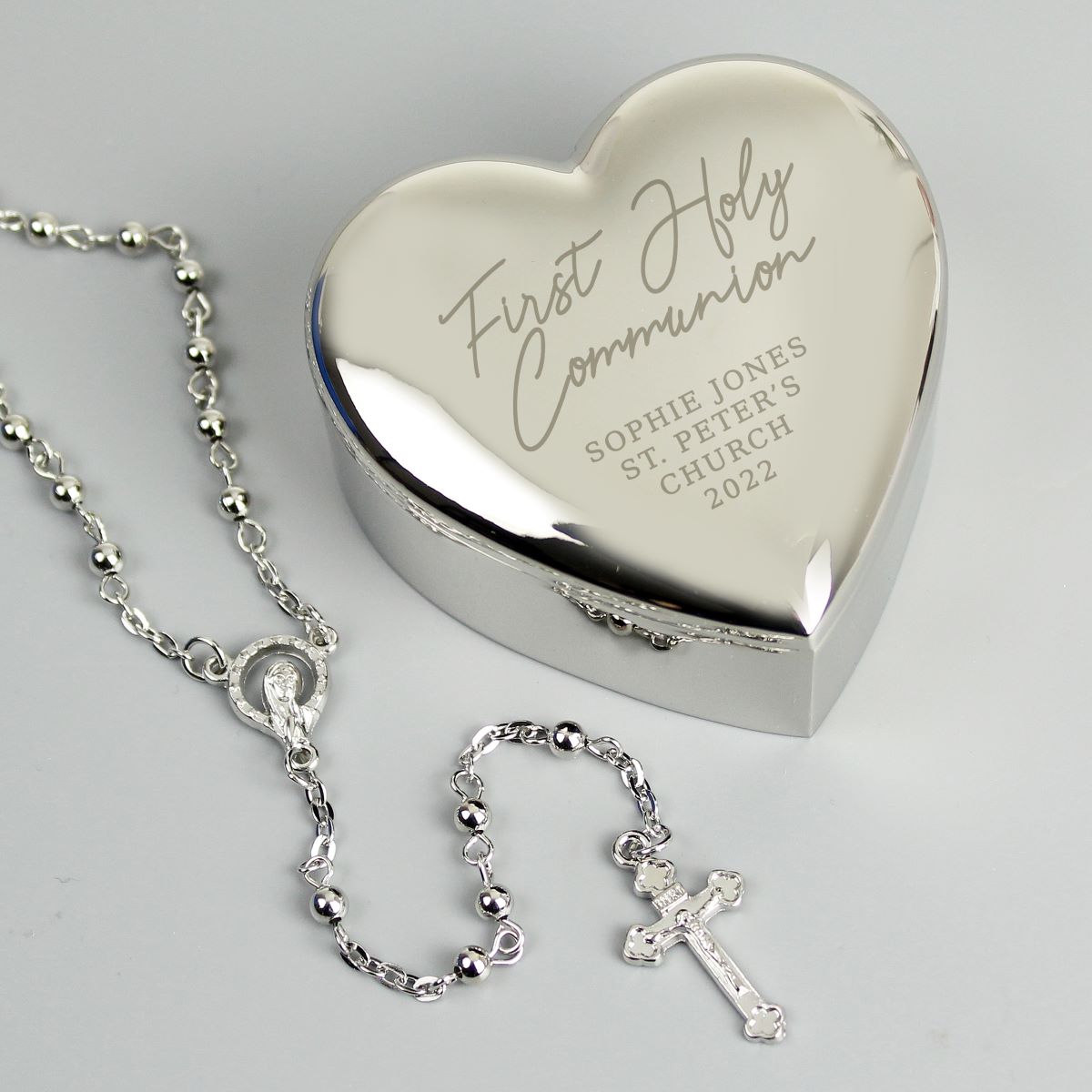 Heart-shaped silver box with engraved text and a silver rosary on a light gray background