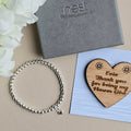 Silver bracelet, wooden heart with engraved message, and Nest box on a beige surface.