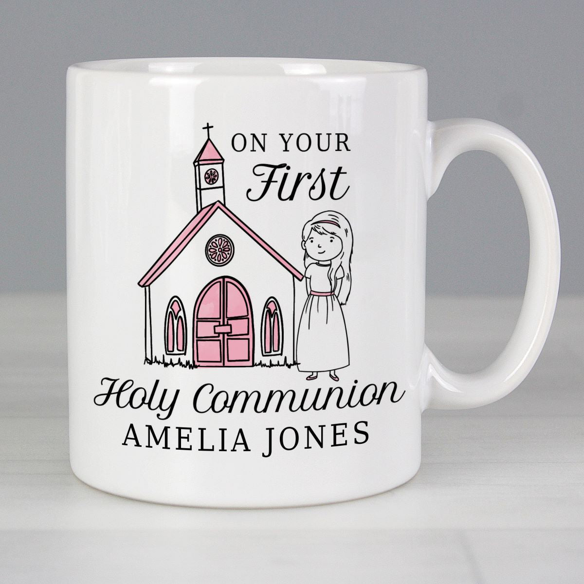 A white ceramic coffee mug with a custom Holy Communion design featuring a pink church illustration, a cartoon girl in a dress, and the text 'ON YOUR First Holy Communion AMELIA JONES'.