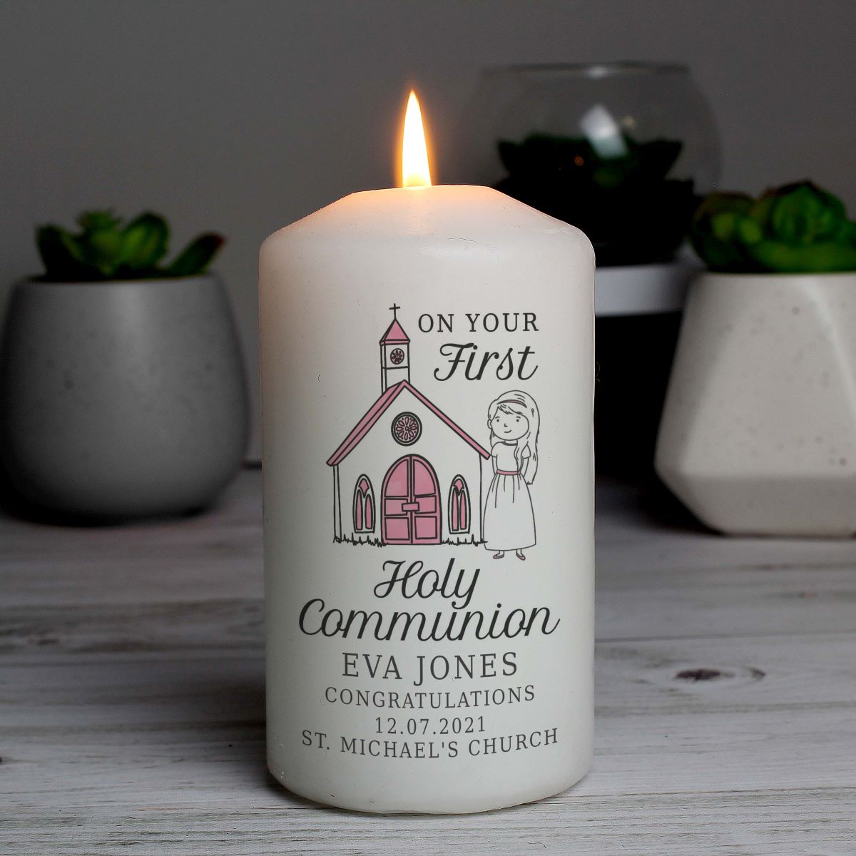 Personalized candle for Holy Communion with a church and person illustration on a wooden surface.