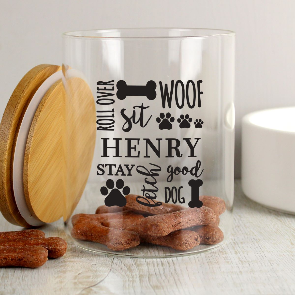 Clear glass jar with wooden lid and dog treats, featuring personalized text on a light background.