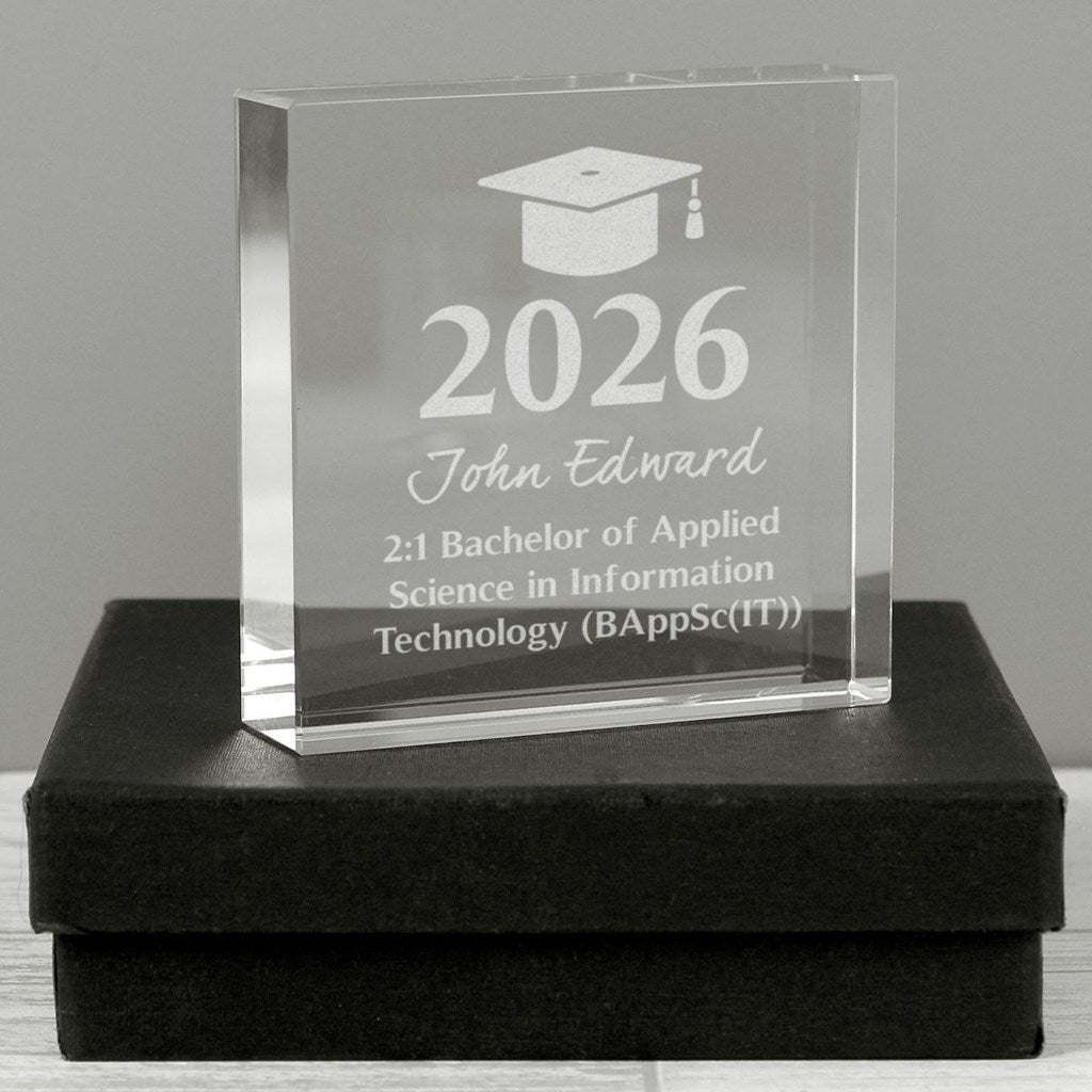 A clear acrylic graduation award block engraved with a graduation cap icon, the year 2026, the name John Edward, and text for a 2:1 Bachelor of Applied Science in Information Technology, displayed on a black presentation box against a gray background.
