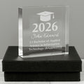 A clear acrylic graduation award block engraved with a graduation cap icon, the year 2026, the name John Edward, and text for a 2:1 Bachelor of Applied Science in Information Technology, displayed on a black presentation box against a gray background.