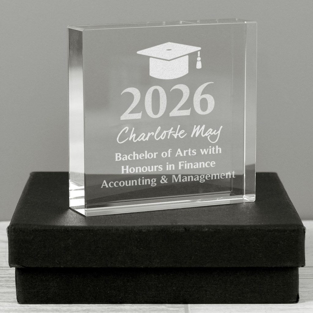 A clear acrylic graduation award block engraved with a graduation cap icon, the year 2026, the name Charlotte May, and 'Bachelor of Arts with Honours in Finance Accounting & Management,' displayed on a black presentation box against a gray background.