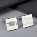 Silver cufflinks with graduation cap icon and engraved text on a gray surface