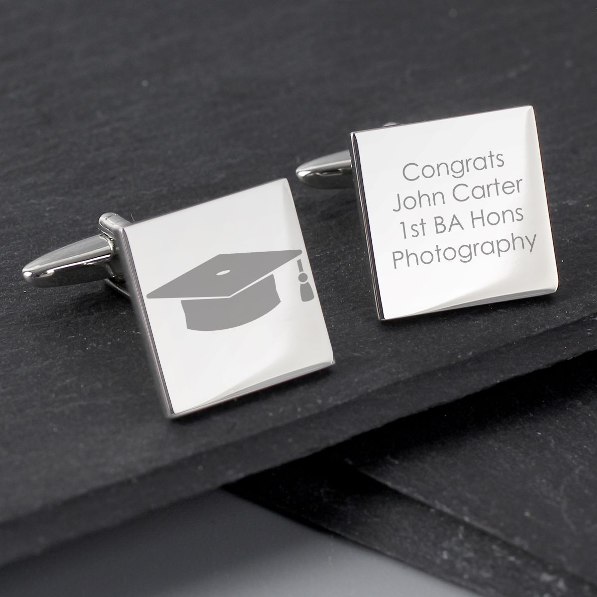 Silver cufflinks with graduation cap design and engraved text on a dark surface