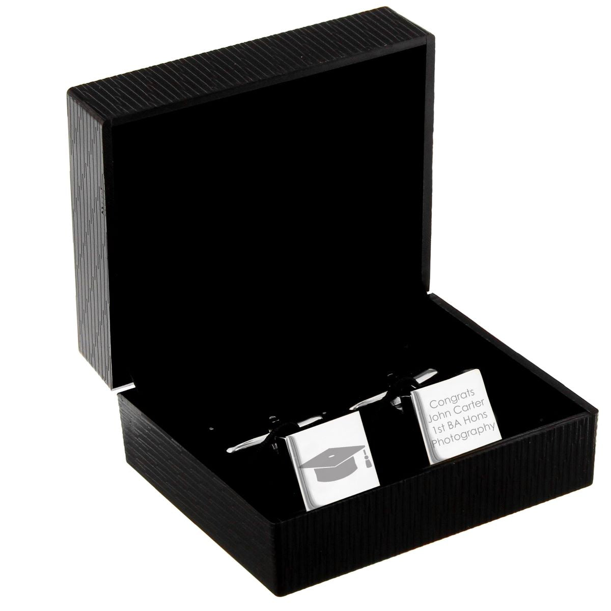 A black ribbed presentation box with its lid open, displaying a silver-toned wedding cufflink and matching rectangular tag engraved with a graduation cap icon and the text 'Congrats John Carter 1st BA Honor Photography'.