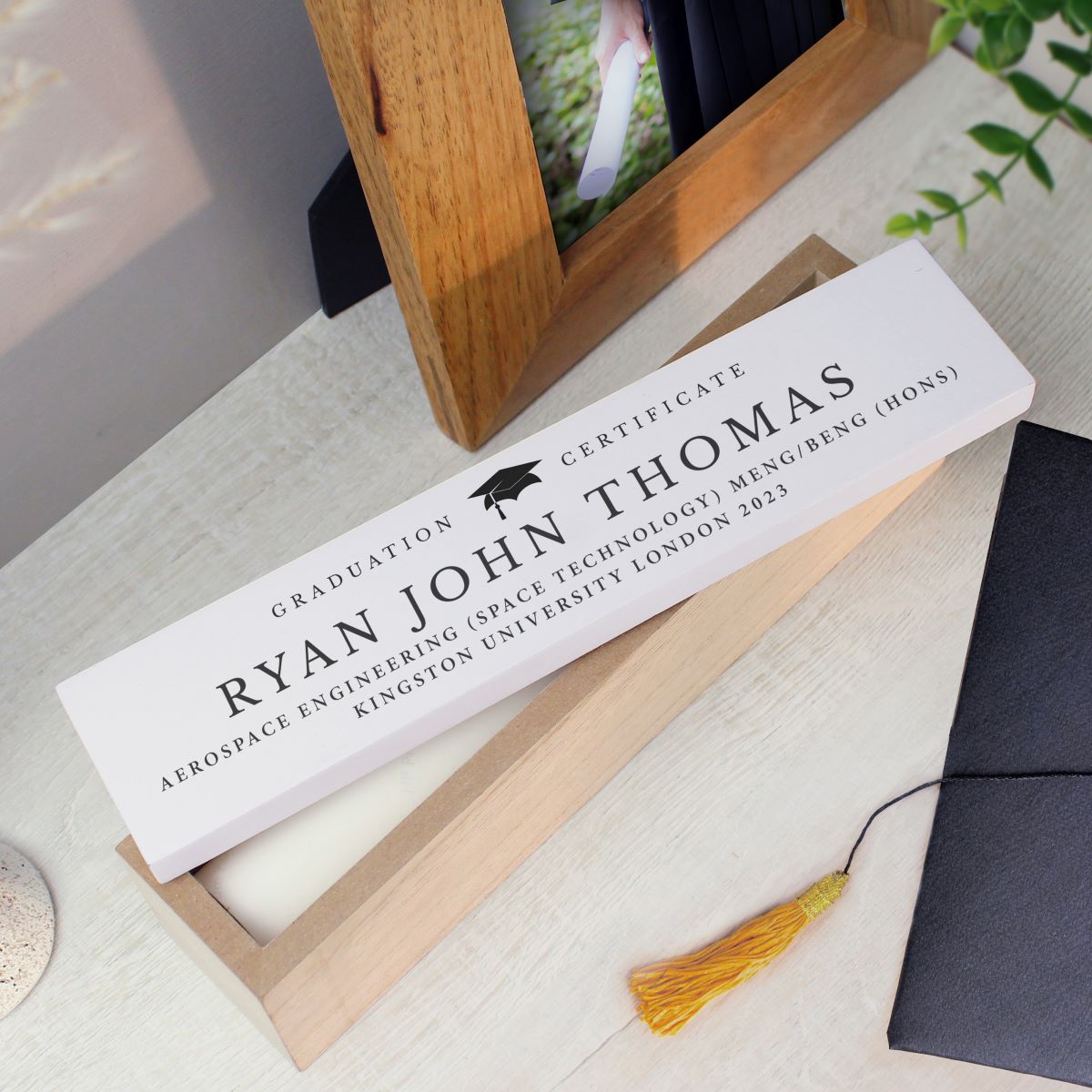 Graduation certificate box personalised for Ryan John Thomas with a tassel on a table.