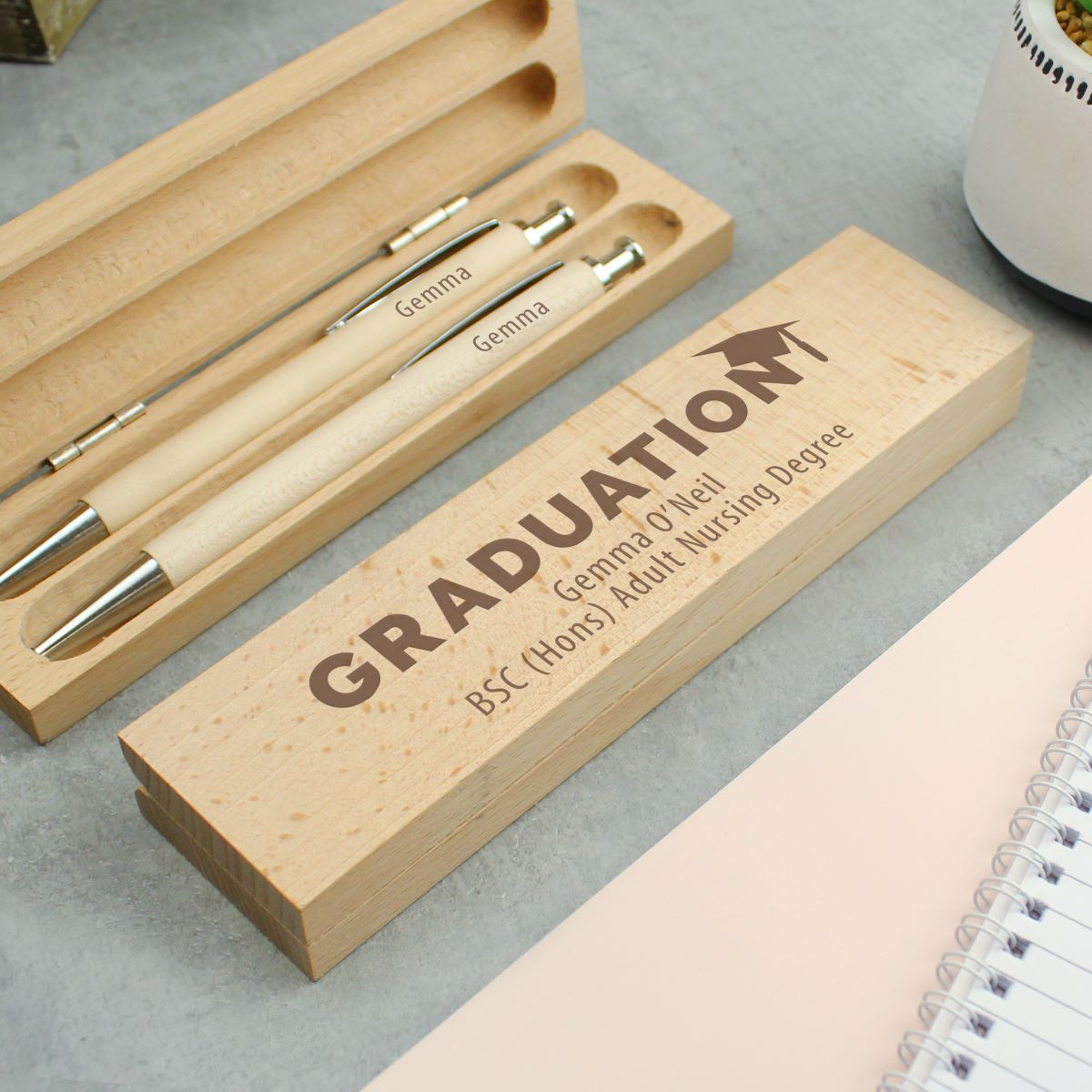Graduation-themed pen set with personalized engraving on a light gray surface.