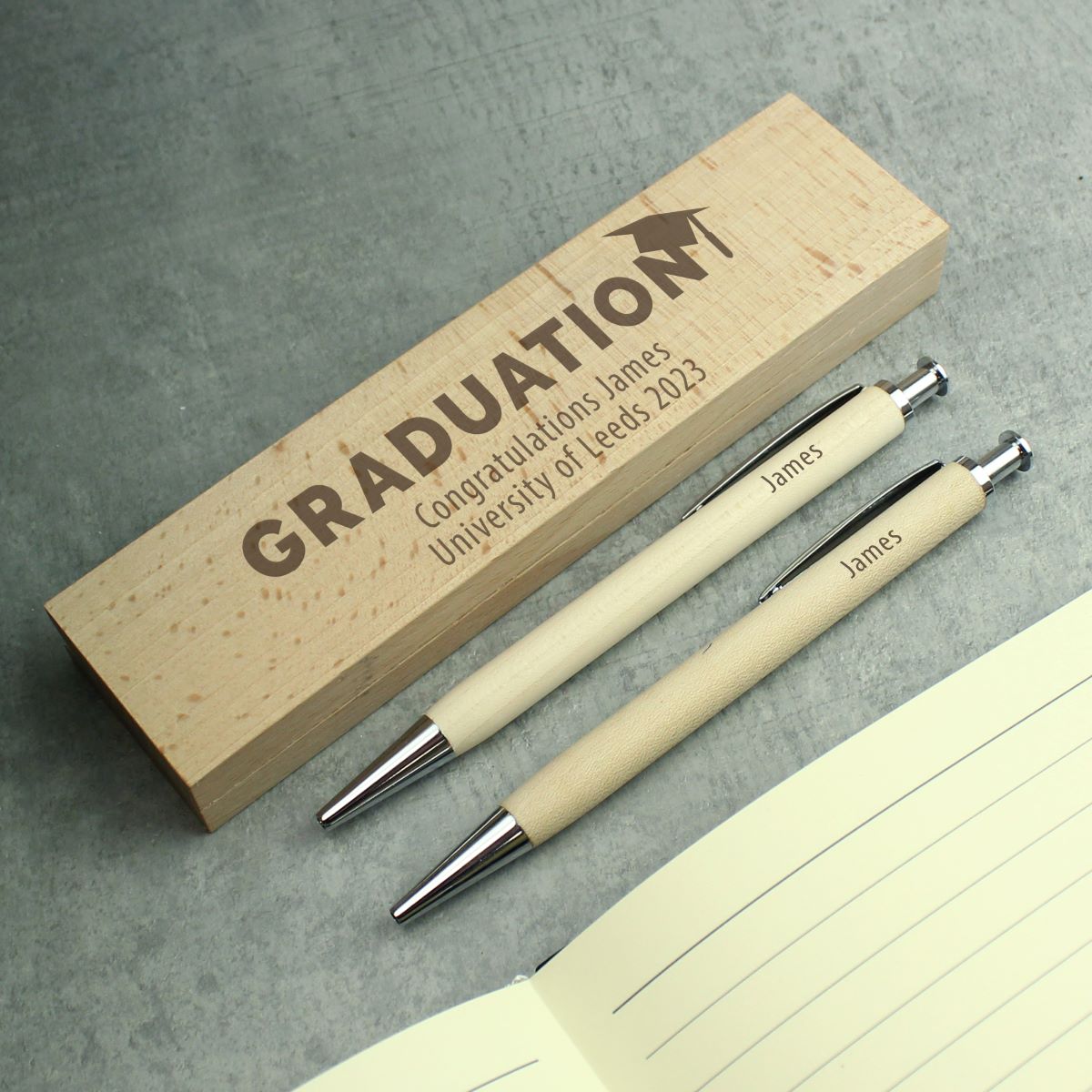 Graduation-themed pen set with wooden box on a gray surface