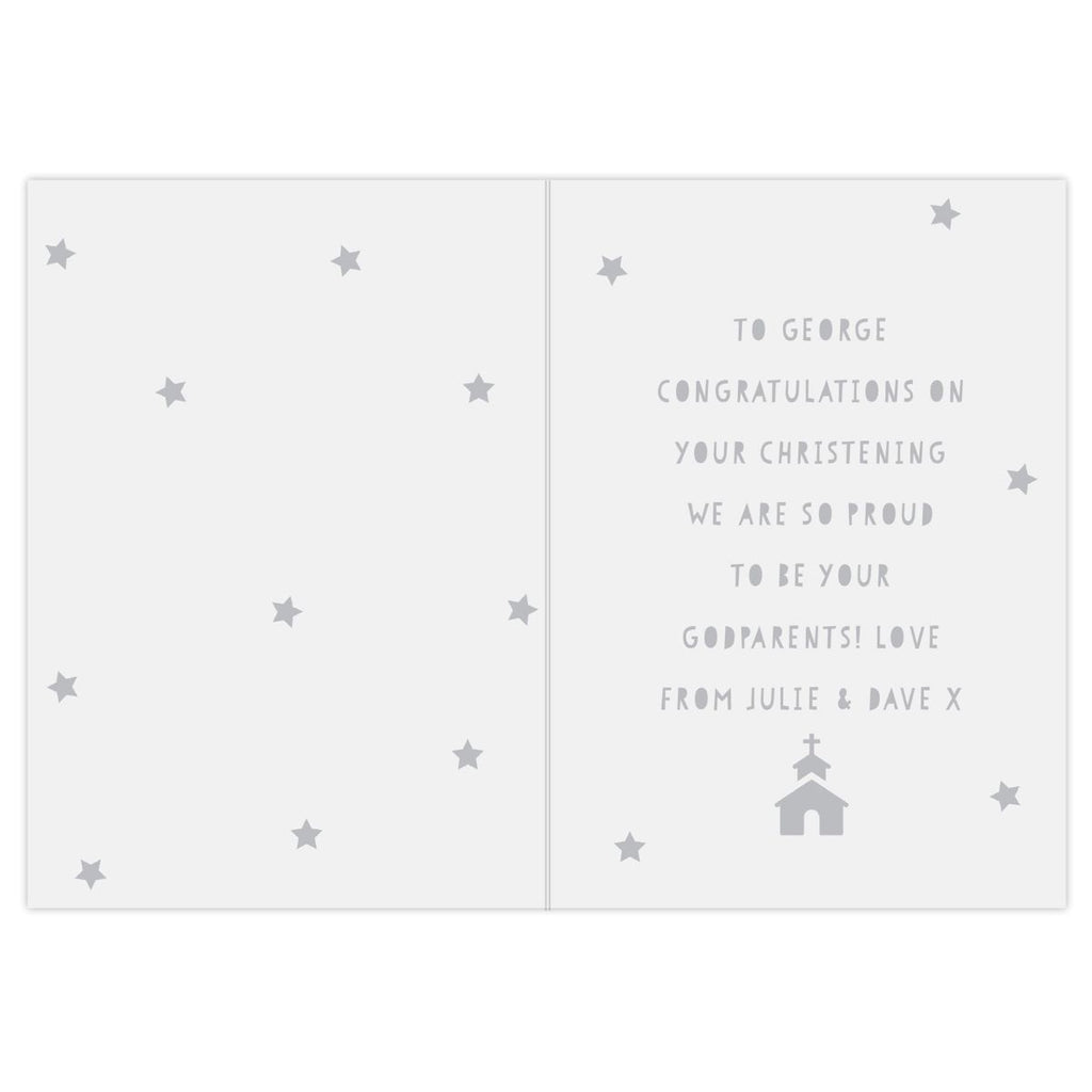 An open folded greeting card with a light gray background and subtle grey star motifs. The right panel contains a personalized message in gray text reading, 'TO GEORGE CONGRATULATIONS ON YOUR CHRISTENING WE ARE SO PROUD TO BE YOUR GODPARENTS! LOVE FROM JULIE & DAVE X,' with a small church icon at the bottom.
