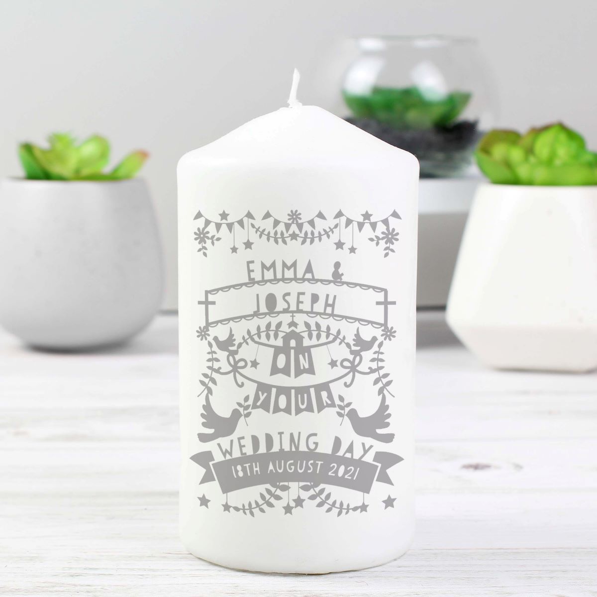 White candle with personalized design in a decorative setting with plants