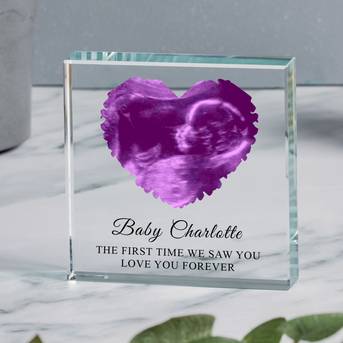 Clear glass block with a pink custom ultrasound image in the shape of a heart and personalised text 'Baby Charlotte THE FIRST TIME WE SAW YOU, LOVE YOU FOREVER' displayed on a Mable surface.