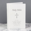 A personalized Holy Bible with a white cover, featuring a silver cross and custom text for a 1st Holy Communion, displayed on a marble surface against a gray background.