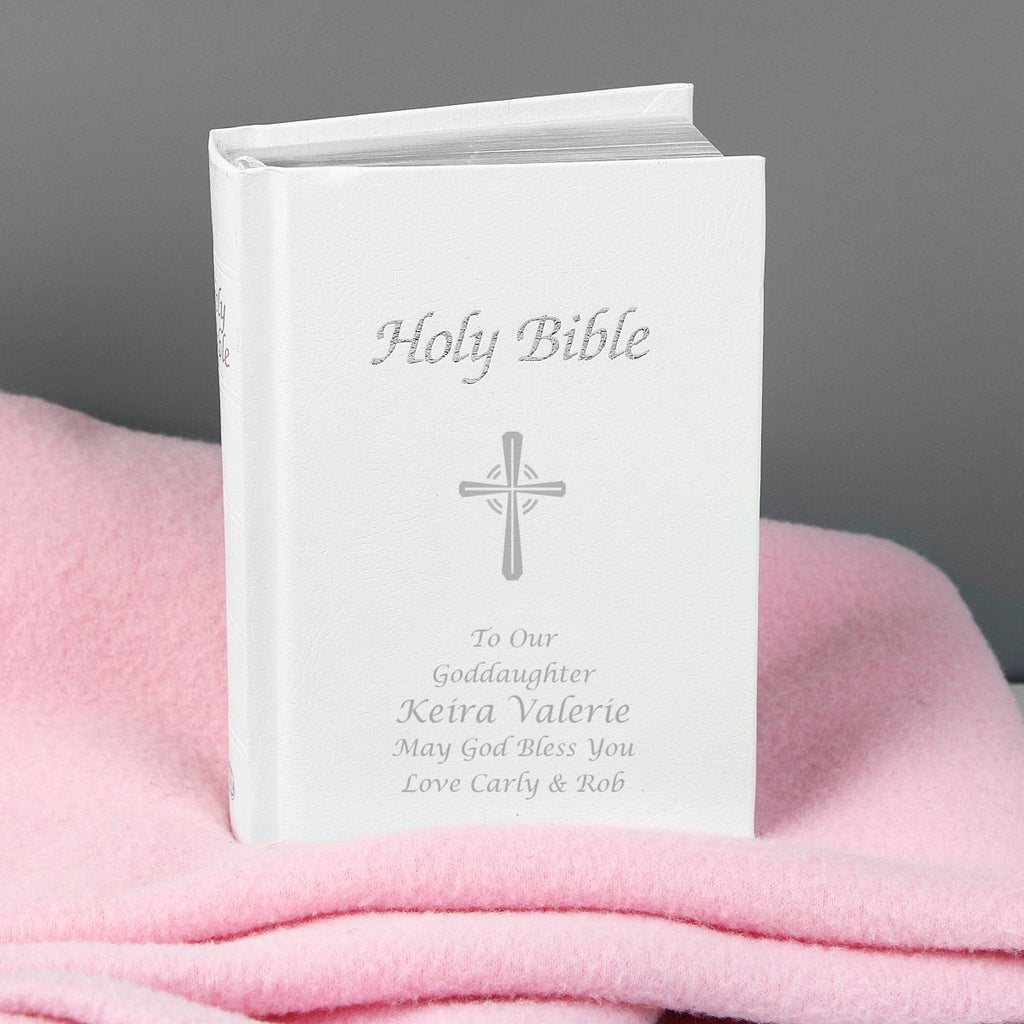 White Bible with engraved text and cross on a pink blanket