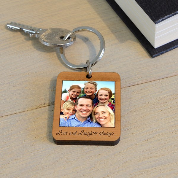A wooden keychain with a family photo and text 'Love and Laughter always...', displayed on a light wooden surface.