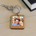 A wooden keychain with a family photo and text 'Love and Laughter always...', displayed on a light wooden surface.