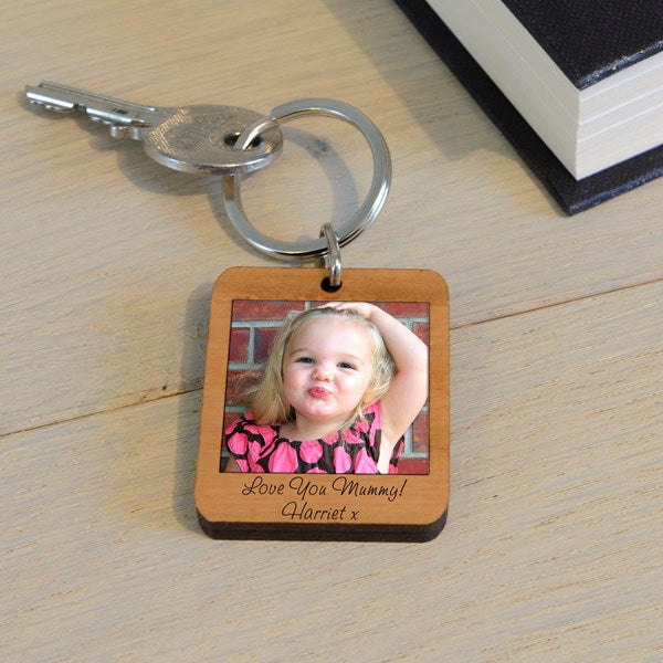 A wooden keychain with a photo of a little girl and text 'Love you Mummy!  Harriet', displayed on a light wooden surface.
