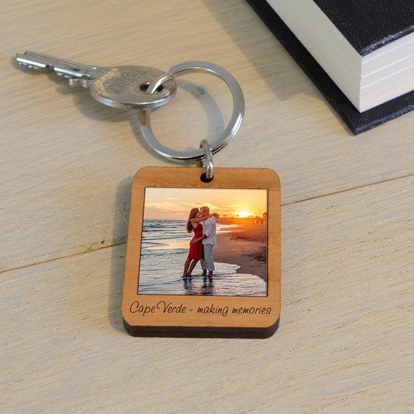A wooden keychain with a photo of a couple of people on a beach and text 'Cape Verde - making memories', displayed on a light wooden surface.