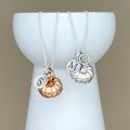 Two silver necklaces with initial charms and pumpkin charms on a white stand against a beige background
