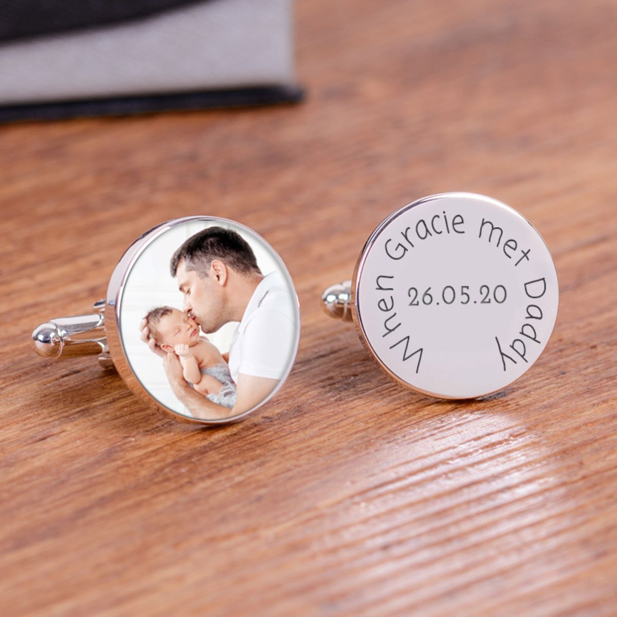 A pair of round silver cufflinks one has a personalised photo and the other one reading 'When Gracie met Daddy' and a date, displayed on a wooden surface.
