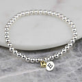 Silver beaded bracelet with a heart-shaped gold charm and a letter 'E' charm on a marble surface.