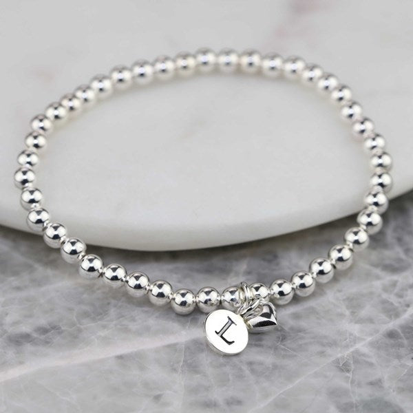 Silver beaded bracelet with a letter 'L' charm on a marble surface