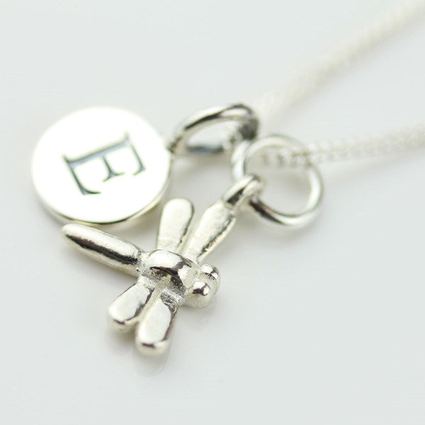Silver necklace with a dragonfly charm and letter 'E' charm on a white background