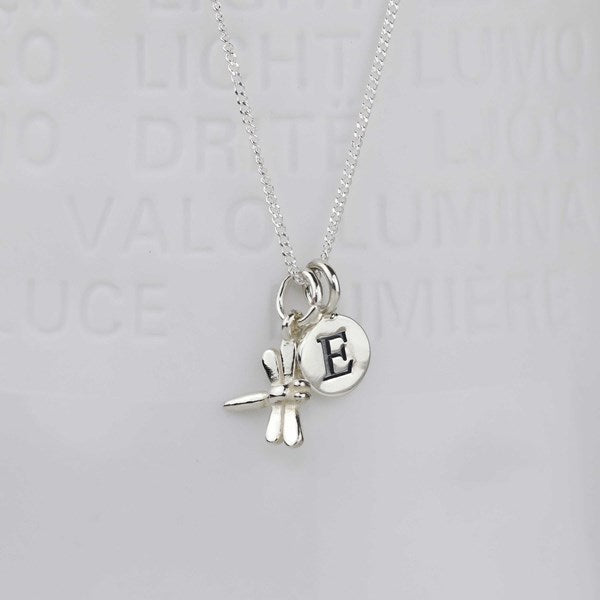 A silver necklace featuring a dragonfly charm and a round initial pendant engraved with the letter 'E', displayed against a light gray background with faint text.