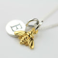 Gold bee charm on a silver chain against a white background