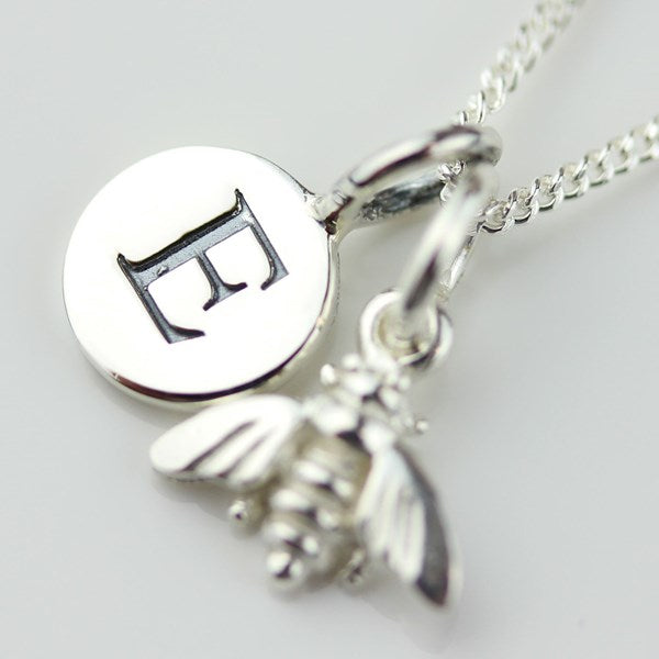 A sterling silver necklace featuring a round disc pendant engraved with a stylized letter 'E', alongside a dangling bee charm, on a matching chain.