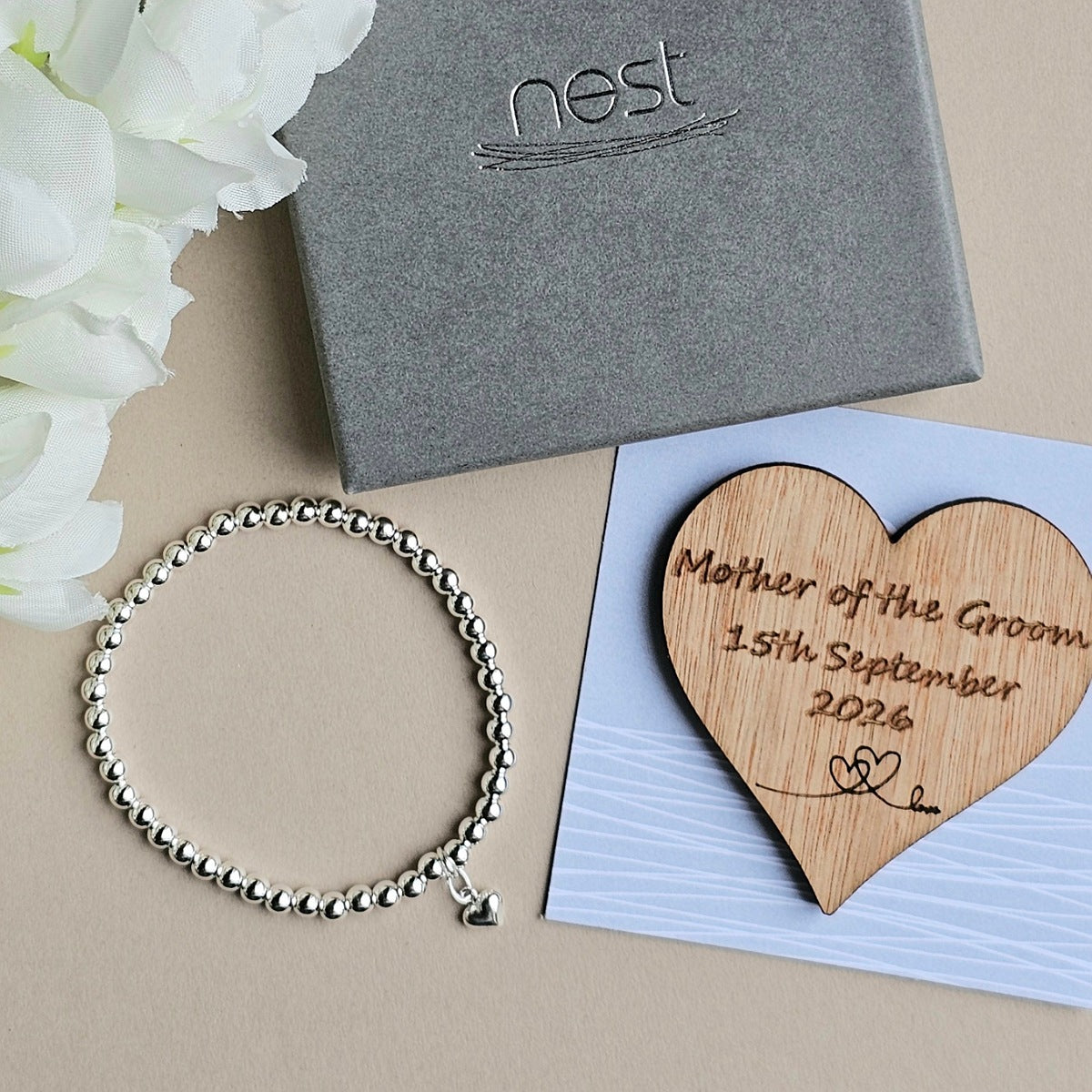Silver bracelet, wooden heart with engraving, and Nest box on a beige surface.