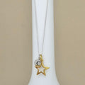 A delicate necklace with a silver chain, featuring a gold star pendant and a small silver disc charm engraved with the letter 'C', displayed on a white jewelry bust against a beige background.