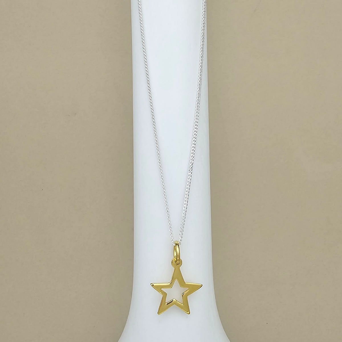 A gold star-shaped pendant necklace on a delicate silver chain, displayed on a white jewelry bust against a neutral beige background.