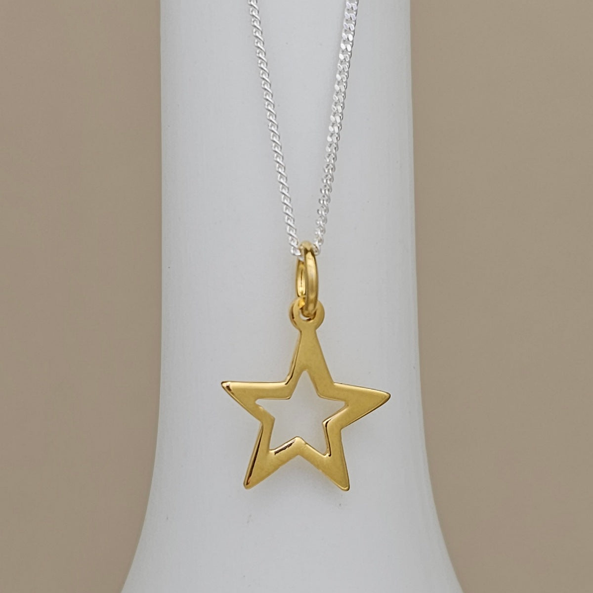 A gold star-shaped pendant necklace on a silver chain, displayed on a white jewelry bust against a neutral beige background.