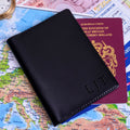 A black passport cover with custom  initials 'LJT', shown on top of a passport and a map.