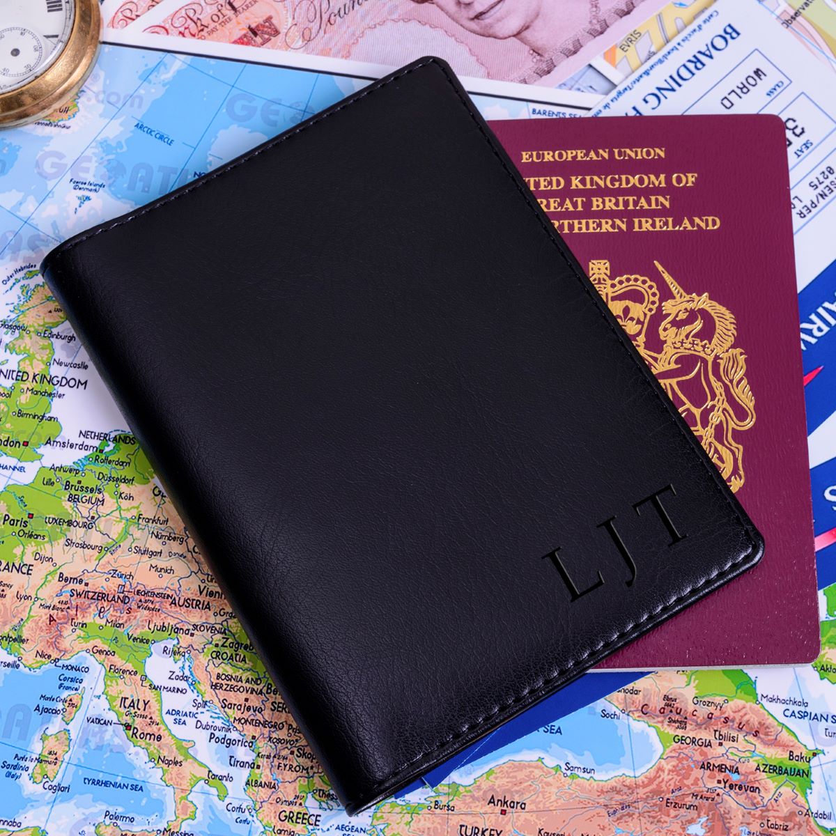A black passport cover with custom  initials 'LJT', shown on top of a passport and a map.