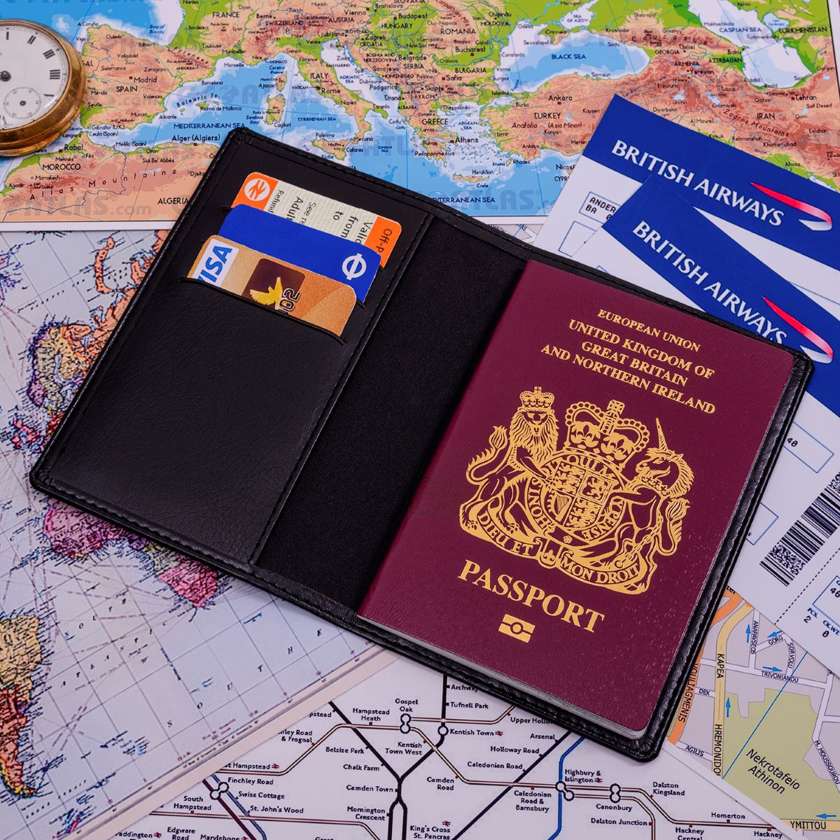 A black passport cover wallet shown open, containing a British passport, credit cards, and travel documents, placed on top of a world map with a British Airways ticket visible.