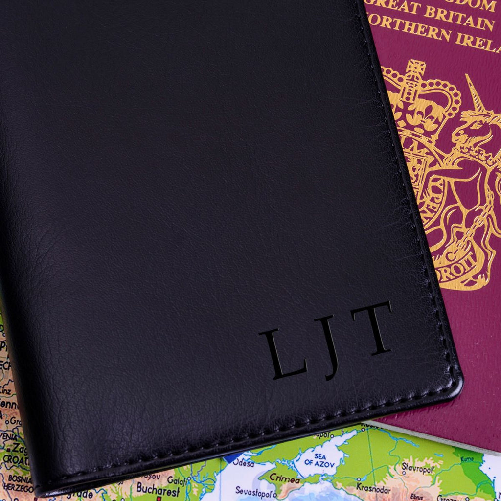 A black passport cover with custom  initials 'LJT', shown on top of a passport and a map.