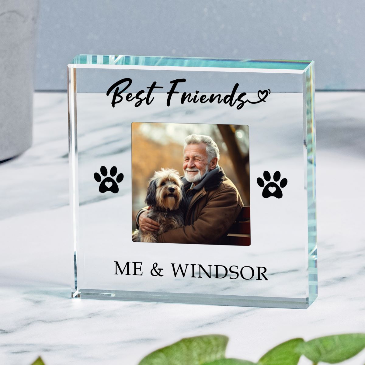 A clear glass  keepsake plaque engraved with 'Best Friends' and 'ME & WINDSOR' with black paw prints, featuring a custom photo of an older man and his dog, displayed on a marble surface.