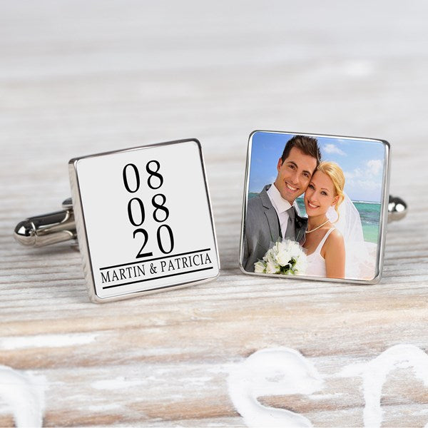 A pair of square silver-toned cufflinks displayed on a light wood surface. One cufflink shows personalised black text on a white background reading '08 08 20 MARTIN & PATRICIA', the other cufflink displays a photo.