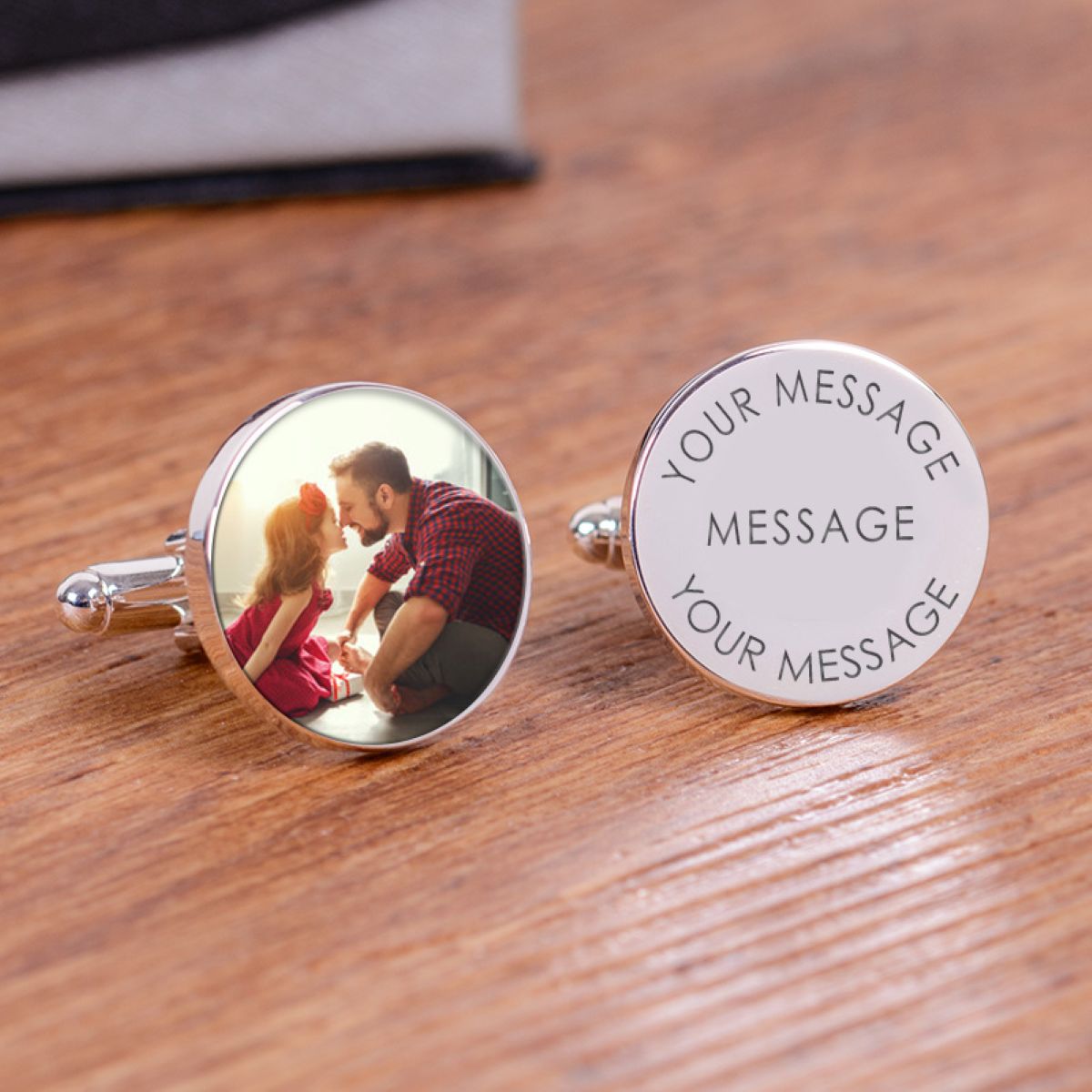 A pair of round silver cufflinks engraved with personalised wording and photo, one reading 'YOUR MESSAGE' and the other a photo, displayed on a wooden surface.