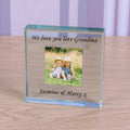A personalized clear glass photo block plaque engraved with 'We love you lots Grandma' and 'Jasmine & Harry x', featuring a custom photo of two children sitting on grass, displayed on a wooden tabletop.
