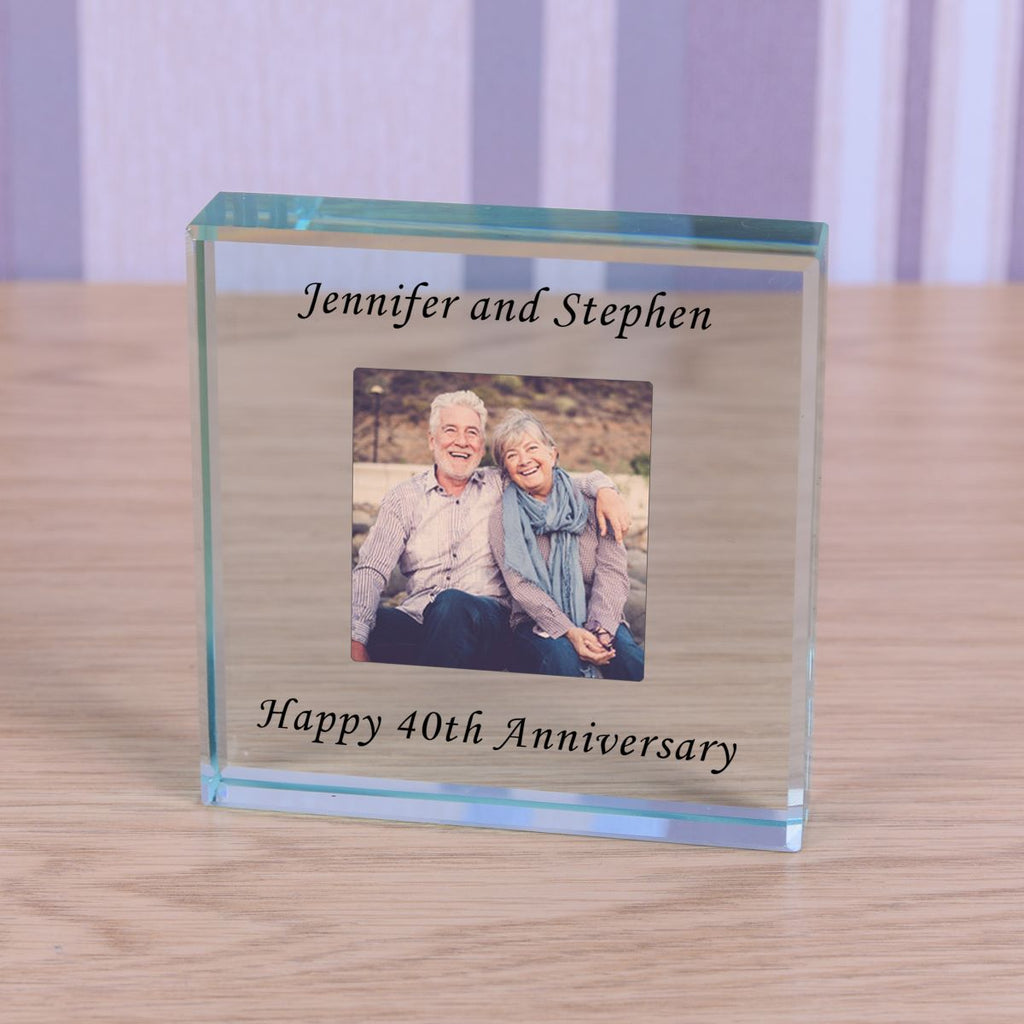 Glass photo block with a picture of an elderly couple and text 'Jennifer and Stephen' and 'Happy 40th Anniversary' on a wooden surface.