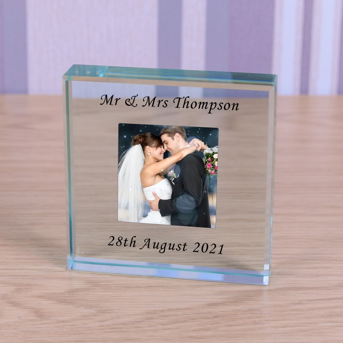Glass photo block with a couple's photo and personalized text on a wooden surface.